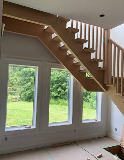 Custom open riser wood staircase installation with solid wood stringers and modern vertical railing in a Simcoe County home