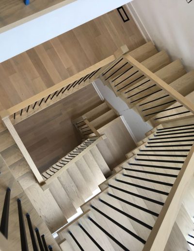 Overhead view of a custom multi-level winding oak staircase with black metal spindles, showcasing expert craftsmanship by Wasaga Stairs.