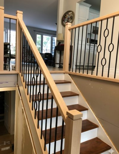 Detailed view of custom light wood railings with decorative circular black metal balusters and stained oak stair treads.
