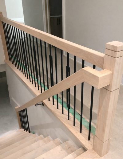 Custom wood stair railing with black iron balusters on an interior landing in Simcoe County