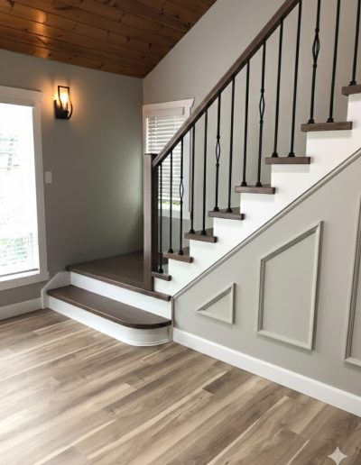 Custom dark oak stair treads with white risers, decorative wall paneling, and black metal spindles in a modern home.