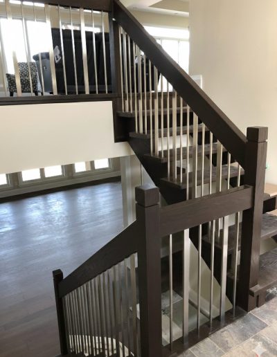 Custom dark-stained oak staircase with modern flat stainless steel spindles and matching wood handrails in a Wasaga Beach home.