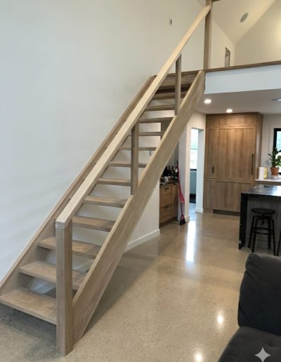 Custom minimalist oak staircase with glass railings leading to a bright open-concept mezzanine in a Wasaga Beach home.