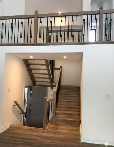 Custom oak staircase with modern black rectangular spindles and matching wood handrails, showcasing a multi-level home design in Wasaga Beach.