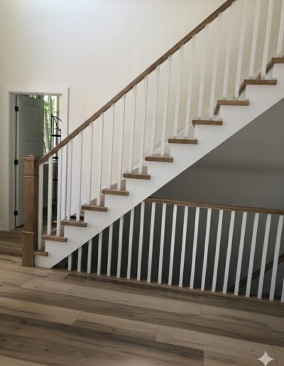 Modern staircase featuring white square spindles, natural oak handrails and treads, and a matching oak newel post over light hardwood flooring.